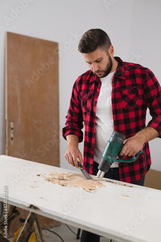 man removing old paint from door with heat gun