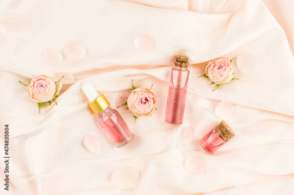 face serum in a glass bottle with a dropper pipette, rose water in a bottle with cork cap on a pink textile background. top view. face serum in a glass bottle with a dropper pipette, rose water in a bottle with cork cap on a pink textile background. top view.