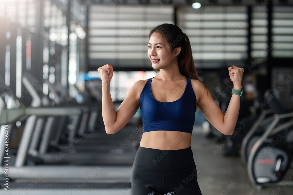 Pretty young Asian woman fit and healthy, raises hands and show muscles, feel proud about her achievement in gym.