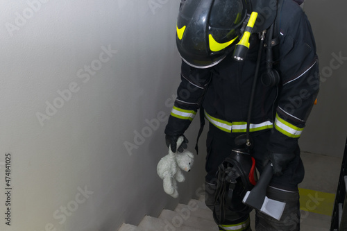 a firefighter climbs the stairs, holding a teddy bear toy and a hatchet for opening doors in his hand photo
