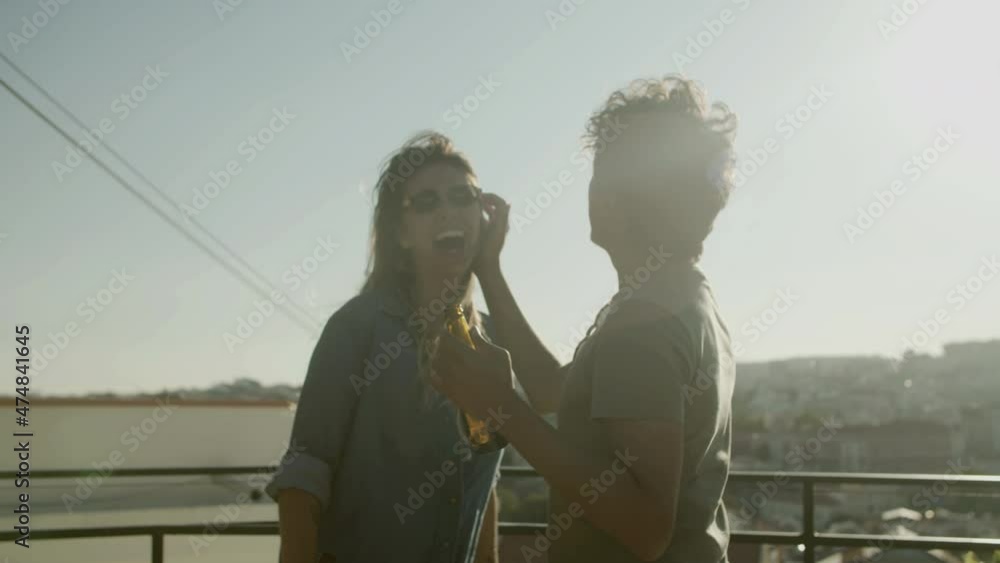 Happy couple of lovers laughing and dancing during rooftop party. Handsome man holding glass bottle of beer, flirting with girlfriends, fixing her hair, having fun together. Love, joy concept Happy couple of lovers laughing and dancing during rooftop party. Handsome man holding glass bottle of beer, flirting with girlfriends, fixing her hair, having fun together. Love, joy concept