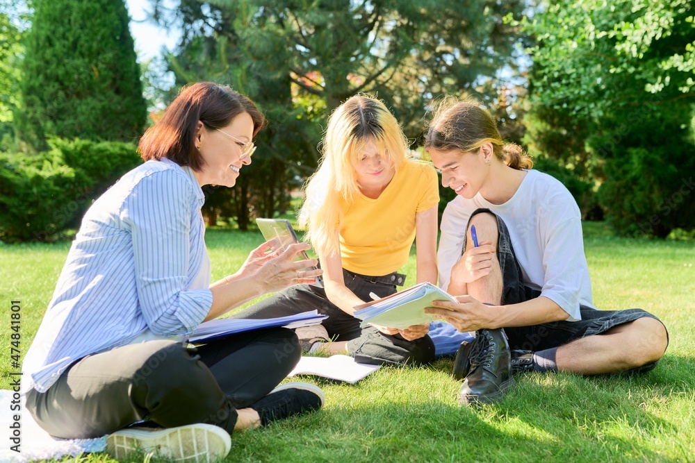 School teacher, psychologist, social worker talking to teenagers, sitting on grass School teacher, psychologist, social worker talking to teenagers, sitting on grass