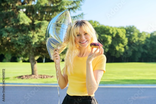 Portrait of beautiful teenage blonde with cake donut and silver balloon in park © Valerii Honcharuk