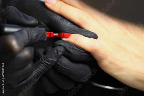 Professional salon worker cover clients nails with red colour polish