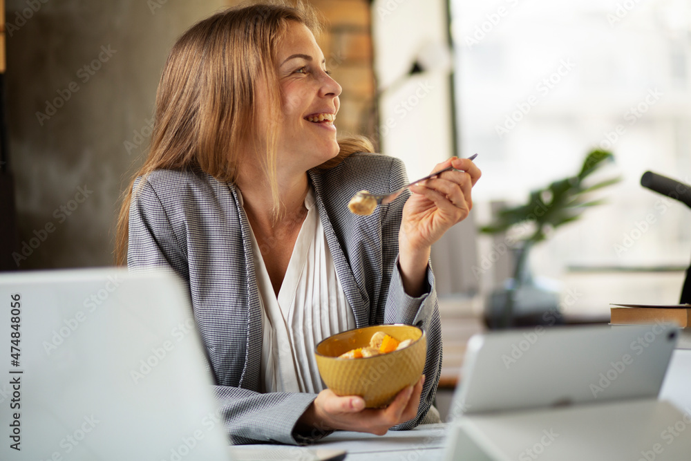 Businesswoman in office having healthy snack. Young woman eating fruit while having a video call. Businesswoman in office having healthy snack. Young woman eating fruit while having a video call.