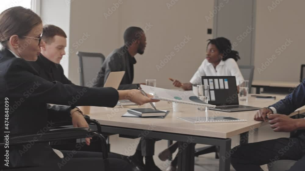 Low angle side view of Caucasian businesswoman with disability passing over documents to African American man, they shaking hands Low angle side view of Caucasian businesswoman with disability passing over documents to African American man, they shaking hands