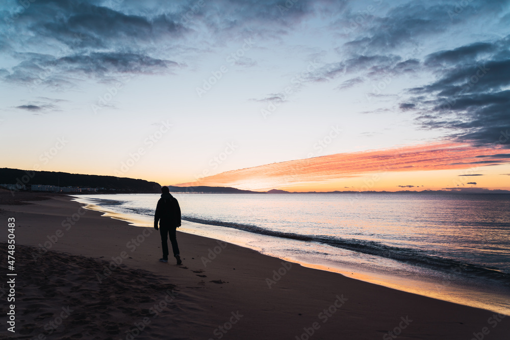 Man walking along a sandy beach during the sunset