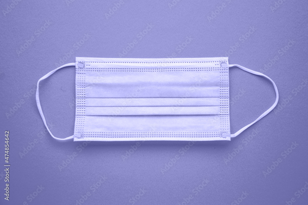A medical disposable mask is isolated on a purple background. Tinting in the trending color of 2022. Very peri. A medical disposable mask is isolated on a purple background. Tinting in the trending color of 2022. Very peri.