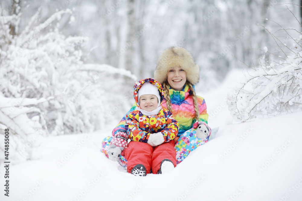 young woman and a young child in a bright colored clothing playing in the winter snow