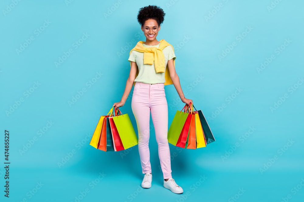 Full size photo of young cheerful african woman hold shopping bags new collection isolated over blue color background Full size photo of young cheerful african woman hold shopping bags new collection isolated over blue color background