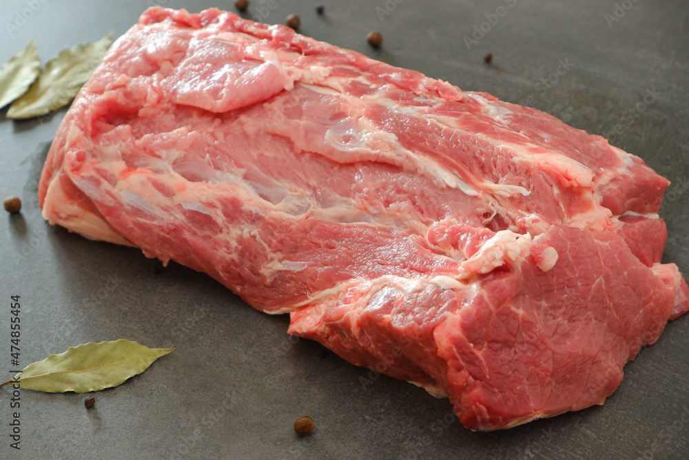 Raw meat. Uncooked fresh pork. A large juicy fresh piece of meat on a gray stone during cooking. Pepper, bay leaf. Culinary concept.