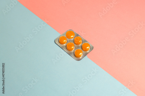 Closeup studio shot of box of orange pills in front of pink blue background, two color backgrounds object , studio photo