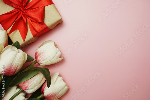 Gift boxes with red ribbon and tulip flower bouquet on pink background