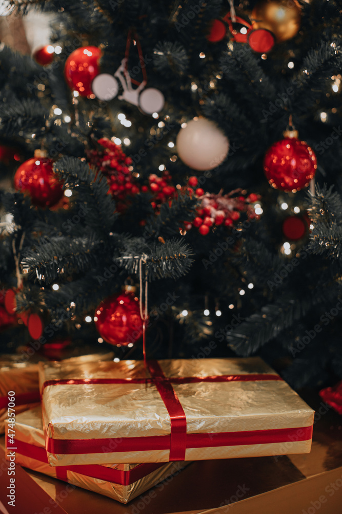 Golden New Year's gift with red ribbon under the Christmas tree. Festive holiday concept and presents Golden New Year's gift with red ribbon under the Christmas tree. Festive holiday concept and presents