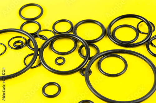 Black hydraulic and pneumatic O-rings in different sizes on a yellow background. Sealing gaskets for hydraulic connections. Rubber sealing rings for plumbing.