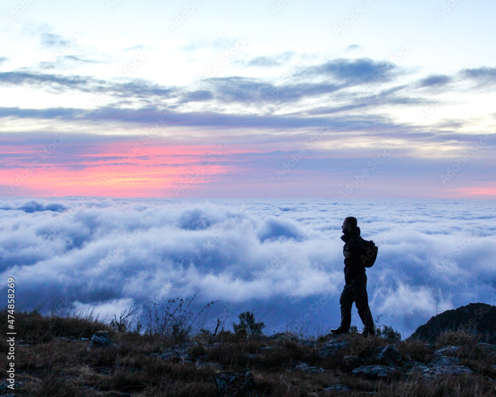 silhueta de homem com mochila nas costas caminhando na montanha ao amanhecer com mar de nuvens ao fundo