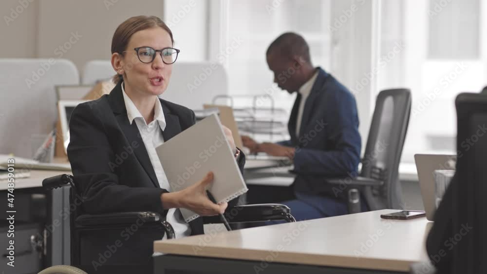 Medium of young female Caucasian accountant wearing formal suit and eyeglasses, holding annual report papers and talking to unrecognizable colleague in office Medium of young female Caucasian accountant wearing formal suit and eyeglasses, holding annual report papers and talking to unrecognizable colleague in office
