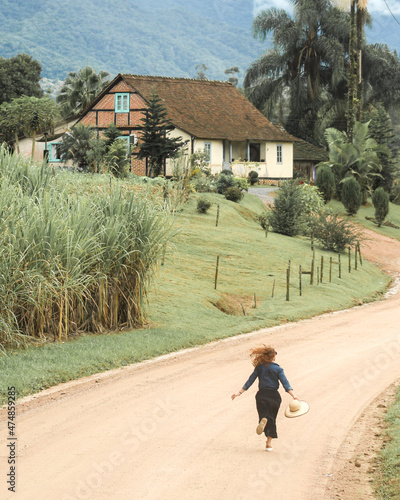 mulher correndo em estrada rural com casa enxaimel ao fundo, em Pomerode, Santa Catarina photo