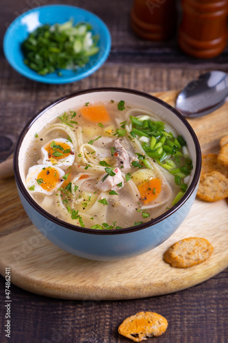 Soup with chicken, noodles, potatoes, quail eggs and carrots. Seasoned with onions and parsley. Close-up.