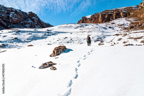 Lonely traveler photographer with backpack climbs the mountains through deep snow