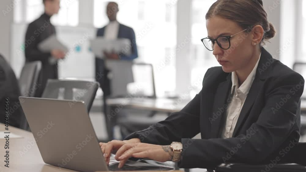 Medium of young Caucasian woman in wheelchair wearing eyeglasses, sitting at desk in office at daytime, typing on portable computer Medium of young Caucasian woman in wheelchair wearing eyeglasses, sitting at desk in office at daytime, typing on portable computer