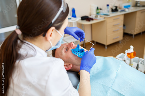 Dentist during the treatment of a male patient. Female dentist in face mask with male patient sitting in dentist chair sitting in dental clinic. Selective focus