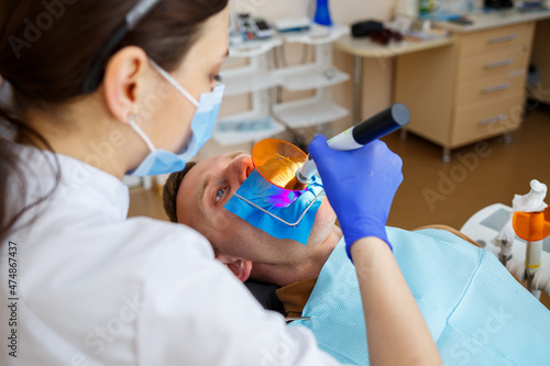 Woman dentist examines the patient with instruments in the dental clinic. The doctor makes dental treatment on the teeth of a person in the dentist's chair. Selective focus