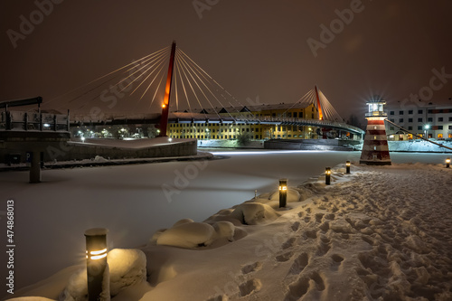 Colorful ship with festive lights frozen in river at Christmas time. Restaurant on water at winter. Pedestrian bridge across the river  in water. Winter landscape with cafeteria in shape of boat.  photo