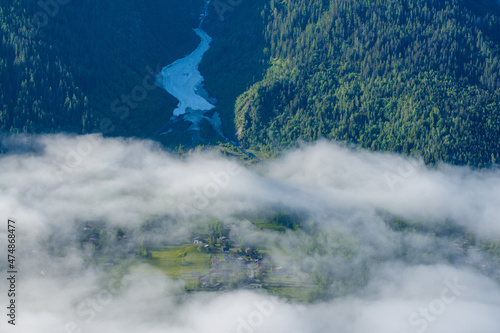 A snowfall between mountains and lush green forests in the Mont Blanc massif in Europe, France, the Alps, towards Chamonix, in summer, on a sunny day.