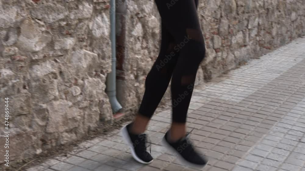 Woman in sports shoes running and exercising on street against stone wall Woman in sports shoes running and exercising on street against stone wall