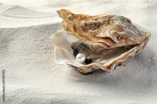 Open oyster with white pearl on sand