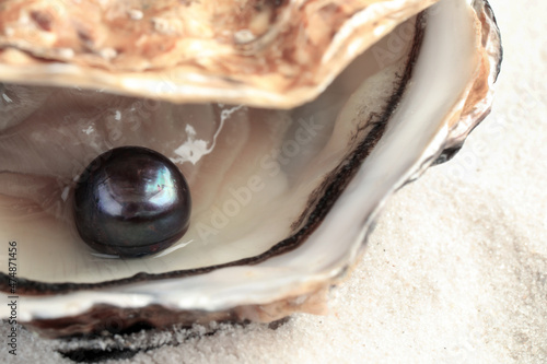 Open oyster with black pearl on sand, closeup