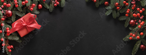 Christmas festive banner with red gift and evergreen nobilis branches on black background with copy space. Xmas greeting card. Winter Holiday. Happy New Year. View from above. photo