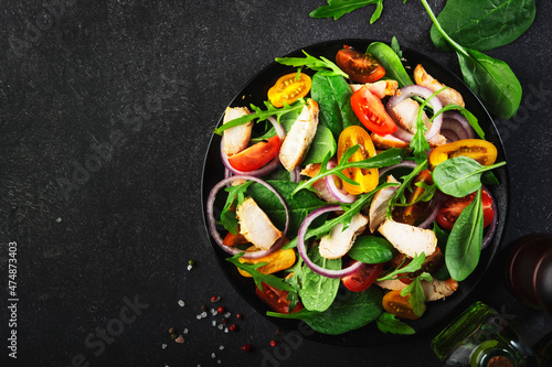 Healthy salad with spinach, grilled chicken, tomatoes, arugula and red onion. Black table, copy space
