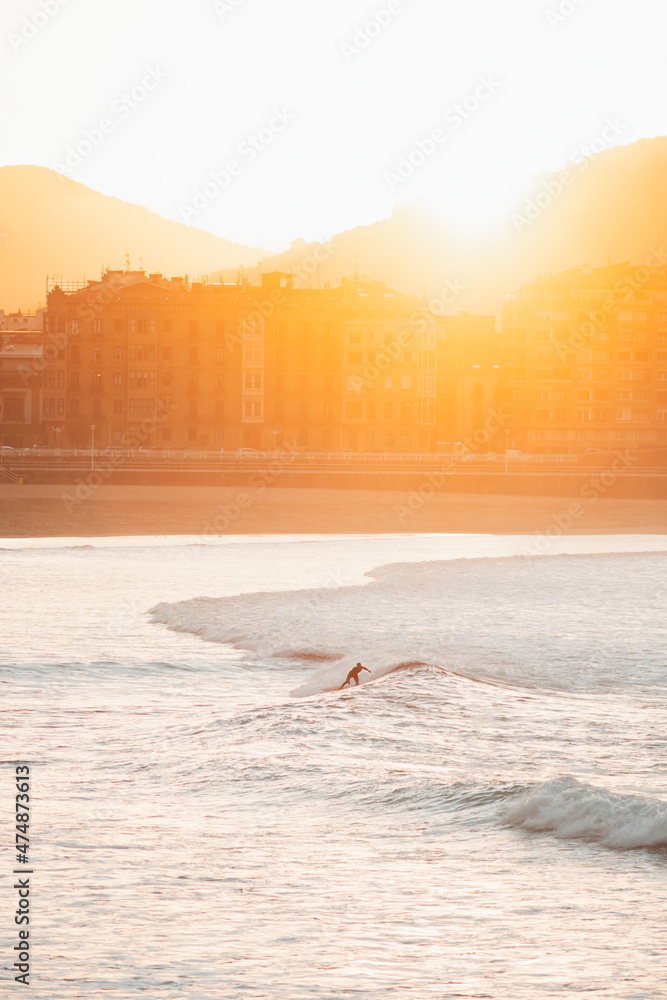Fototapeta premium Silhouette of a lonely surfer riding a wave during sunset in San Sebastian beach