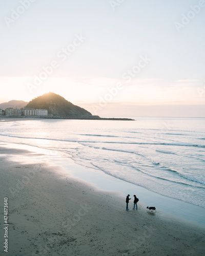 Couple talking on the shore of Zurriola Beach in San Sebastian during sunset while their dog is running around