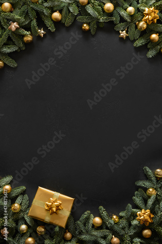 Christmas vertical frame with gold gift, baubles, evergreen branches on black background with copy space. Xmas greeting card. Happy New Year. View from above, flat lay.