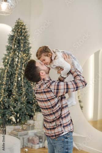 Adorable daughter with her dear father at home in gront of fit tree. Chrisrmas mood photo