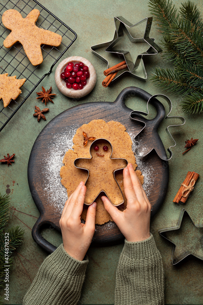 Cooking Christmas cookies, gingerbread man with cutter. Made with hazelnut butter. Christmas and New Year traditions concept, view from above, green background with fir tree brunches. Cooking Christmas cookies, gingerbread man with cutter. Made with hazelnut butter. Christmas and New Year traditions concept, view from above, green background with fir tree brunches.