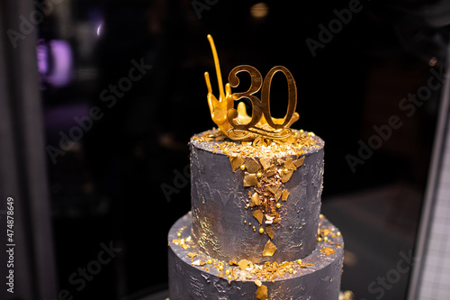 festive two-tier dark cake with gold decoration for the 30th anniversary. candybar for birthday photo