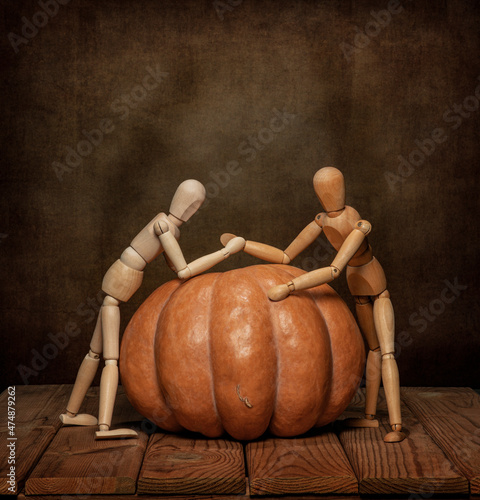 Wooden men play with a pumpkin on Halloween on a wooden table and an artistic background.