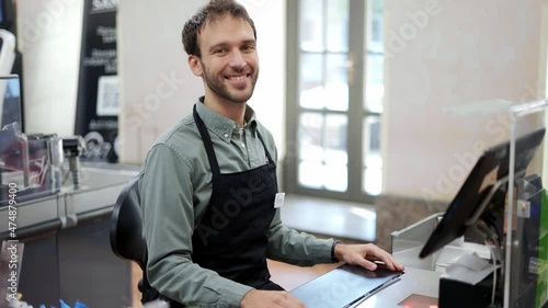 Handsome man in supermarket waiting at cash desk for next customer. Smiling cashier