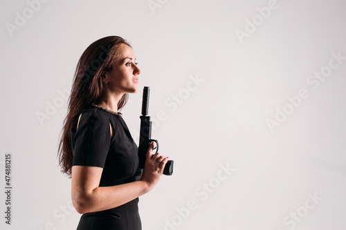 young girl in a black suit with a pistol in her hands on a white background in the studio, she portrays a security guard, bodyguard or agent.