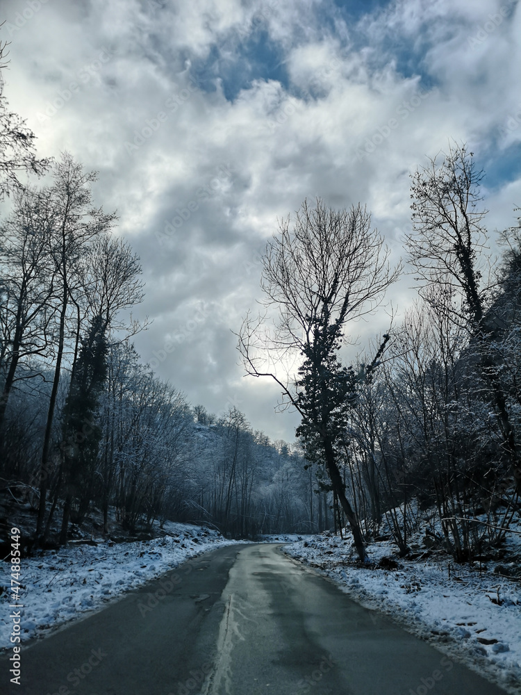 Fototapeta premium Cloudy road high in the mountains while snow storm. Dangerous mountain road with grey cloudy sky.