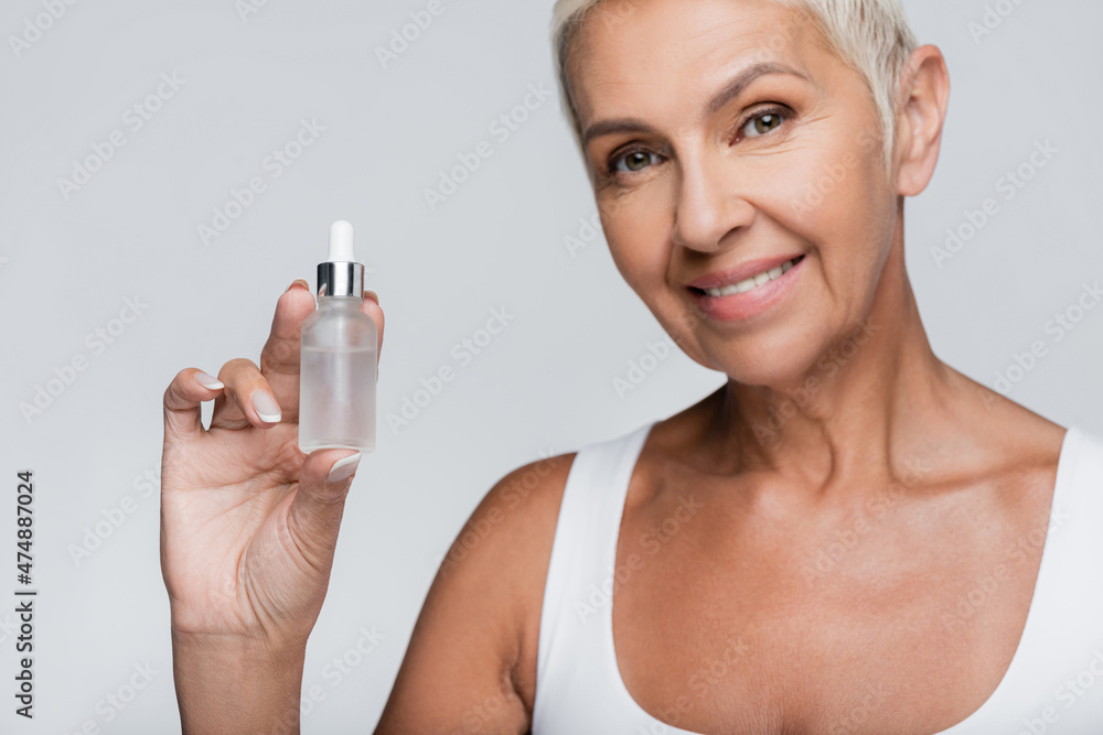 happy elderly woman holding bottle with serum isolated on grey happy elderly woman holding bottle with serum isolated on grey