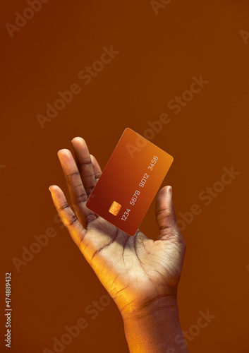 African american female hand holds levitating template Bank credit card with online service on golden orange background