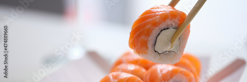 Hand with disposable chopsticks holds sake nigiri sushi with salmon fish