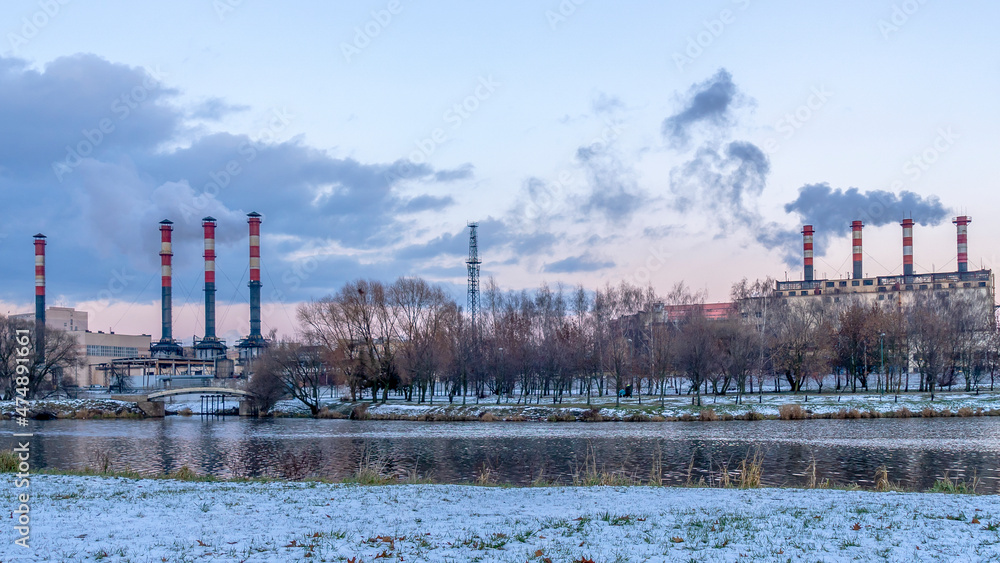 Obraz premium Smoking chimneys of thermal power plants near the waterfront in city. Winter. Industrial and nature background.