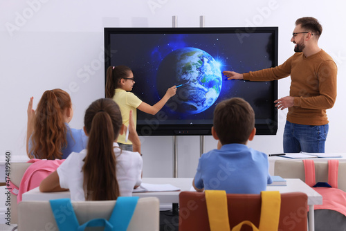 Teacher and pupil using interactive board in classroom during lesson photo
