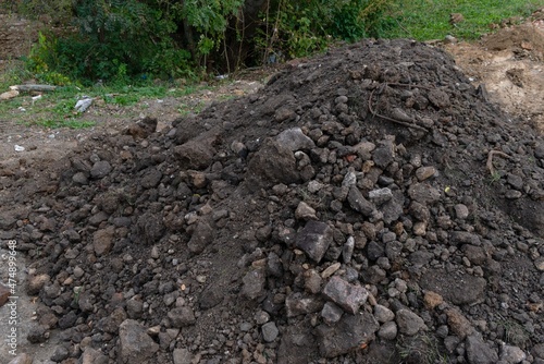 Pile of dark construction gardening soil mud land earth dirt heap pile mound, freshly dug, with some wet soil and leaves 